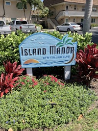 a sign that says island manor in front of bushes and flowers